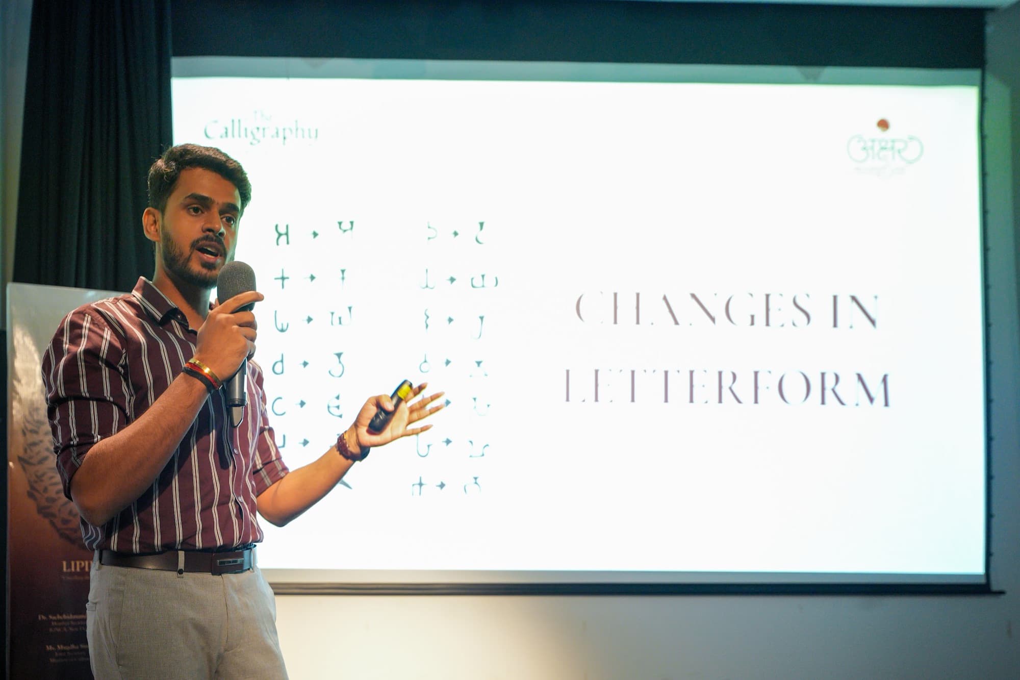 Young speaker with a microphone gesturing in front of a slide reading Changes in Letterform