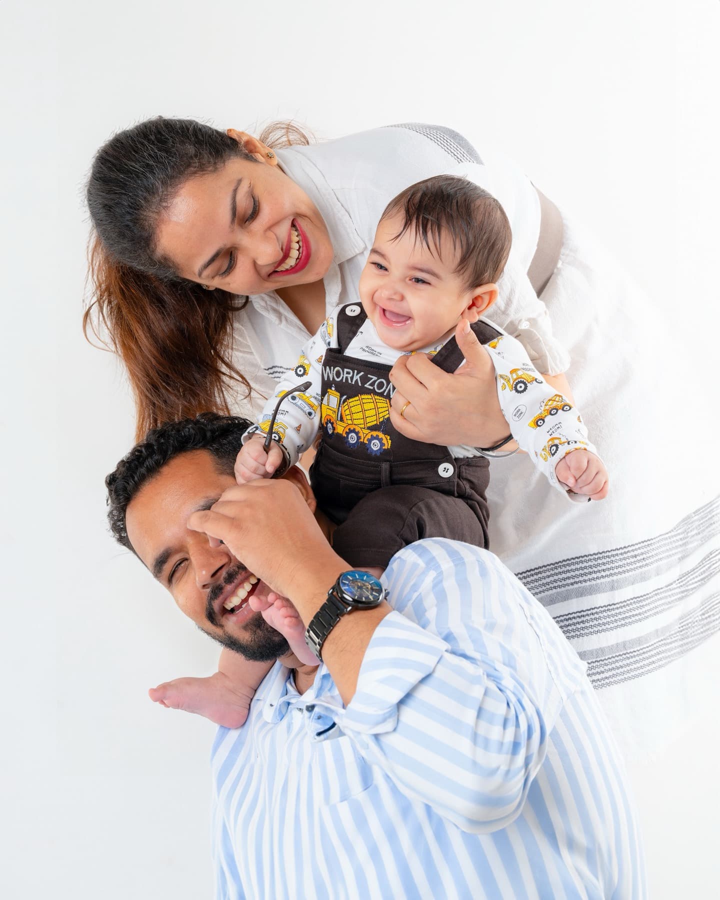 Mother, father and laughing baby packed close together in a tight white-background portrait