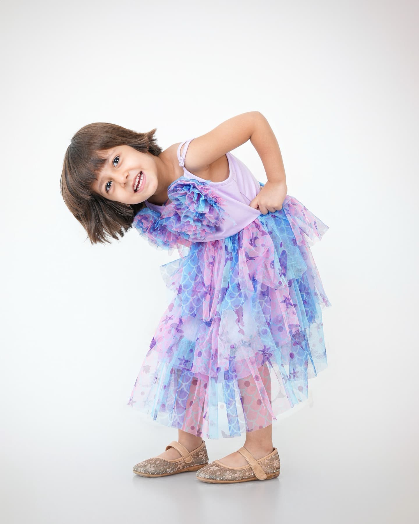 Young girl in a lilac tulle party dress bending toward camera holding out her skirt