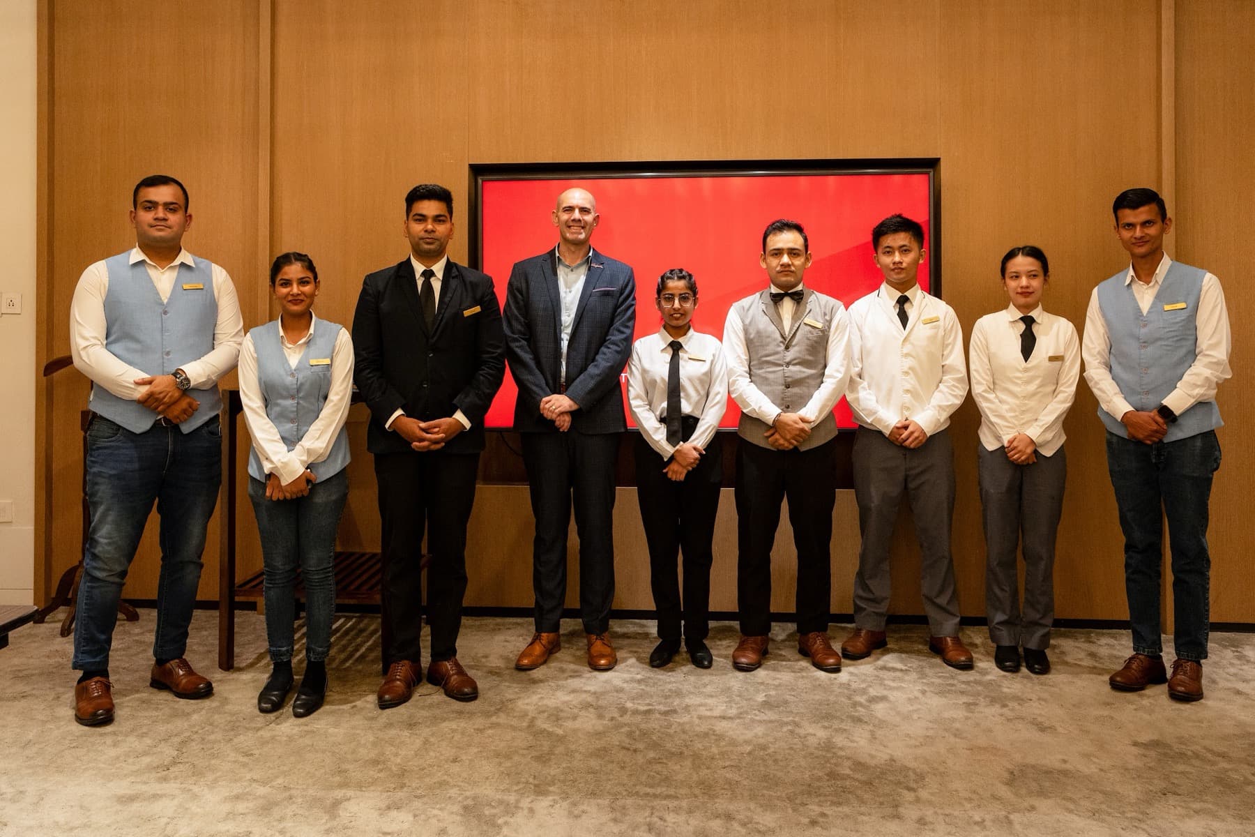 Row of ten hotel staff and a manager posed in a line in front of a red-lit screen