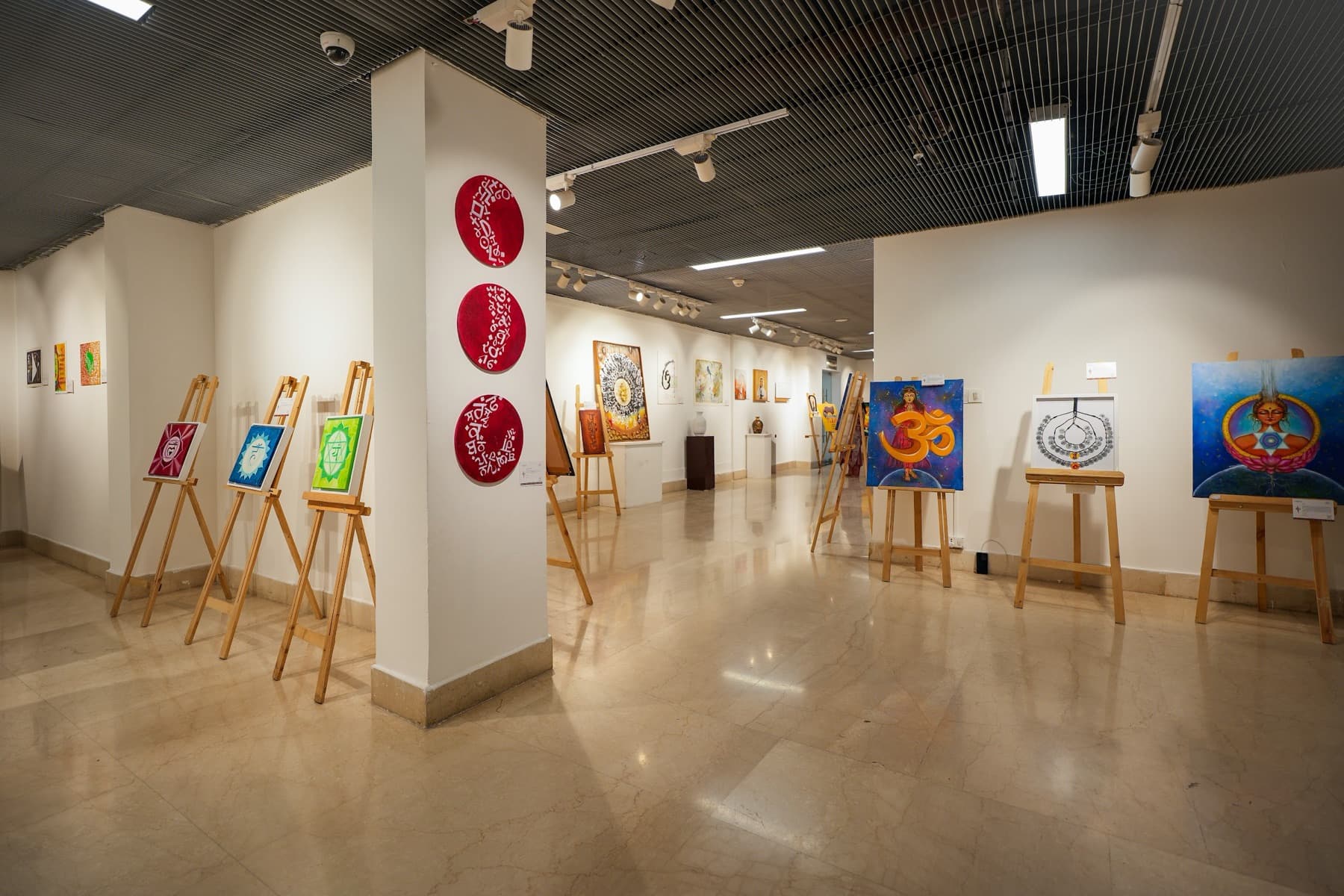 Gallery room with paintings on wooden easels and red circular calligraphy discs on a pillar