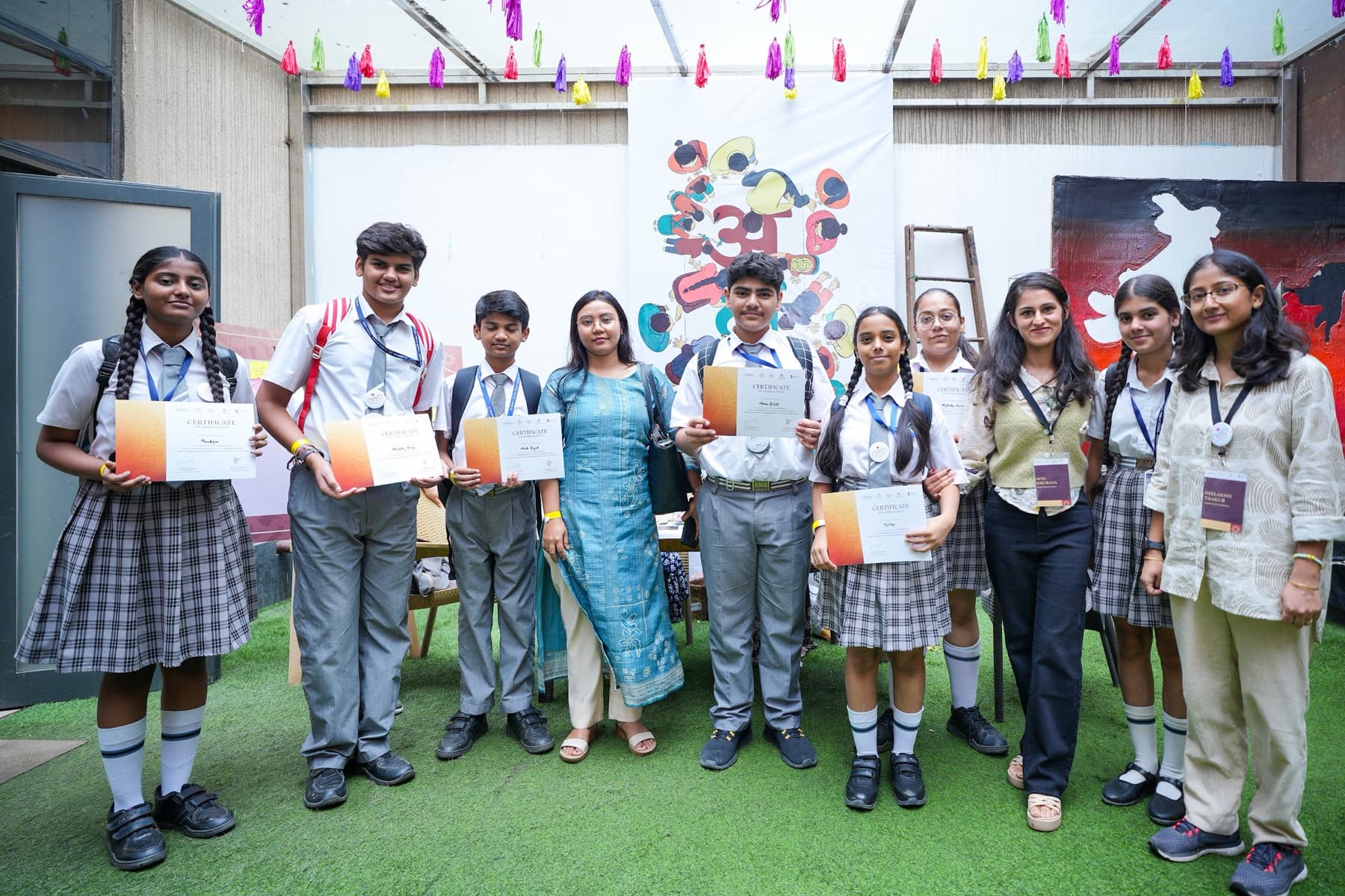 School students holding certificates posed with two organisers under colourful tassel bunting