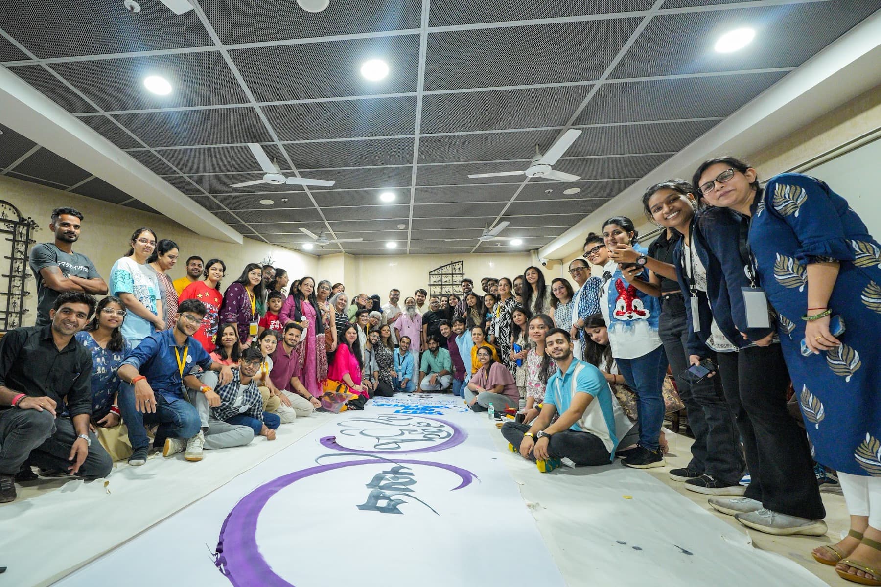 Large group of workshop participants posed behind a finished purple calligraphy canvas on the floor