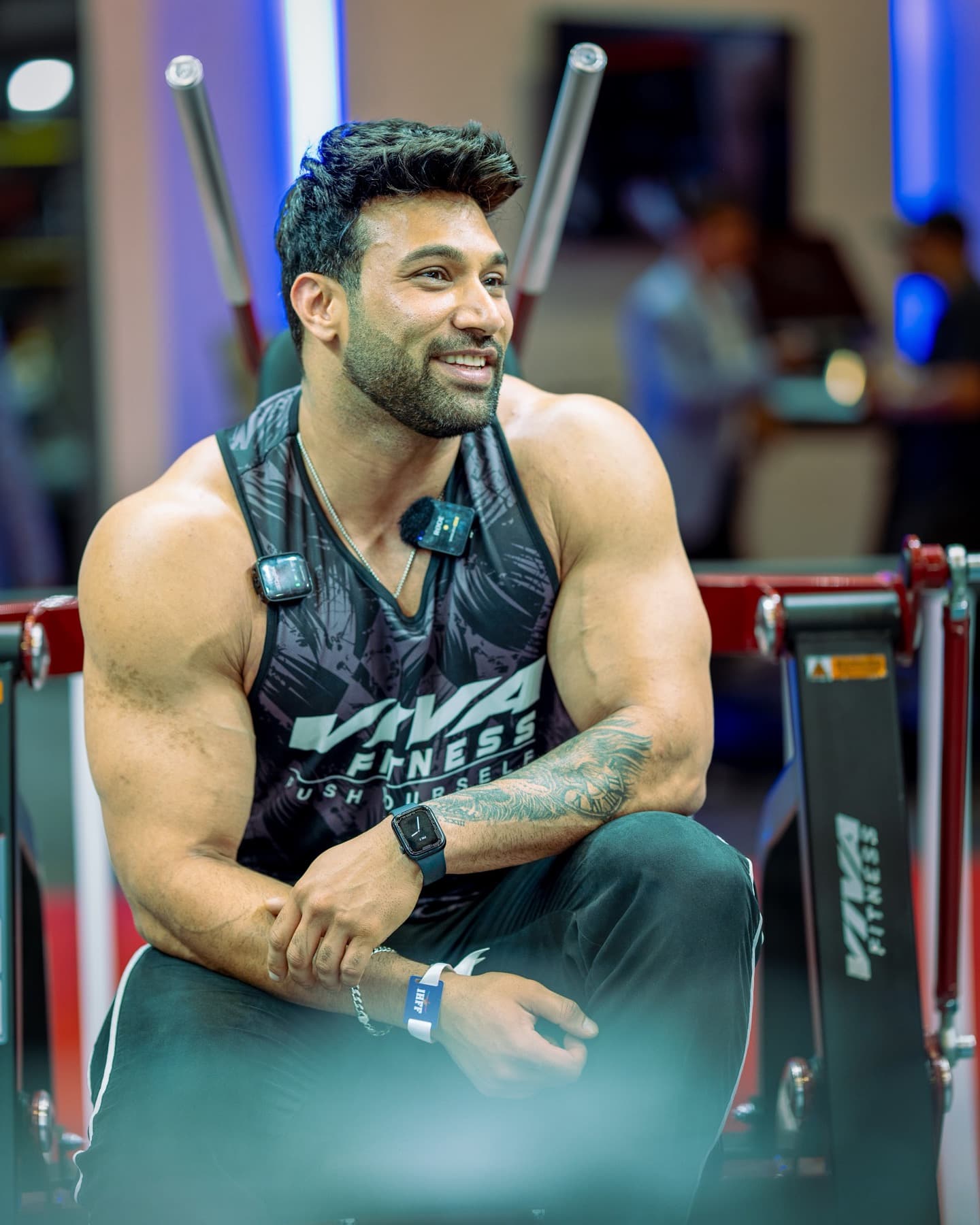 Smiling muscular man sitting on a gym machine looking off to the side