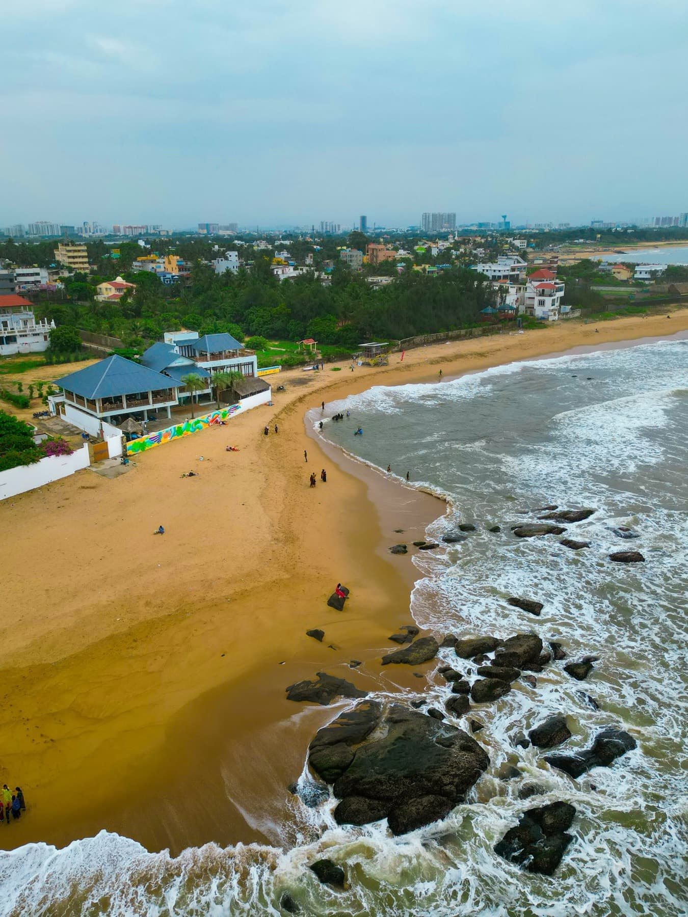 Drone view of a beach, rock groyne and breaking waves beside a coastal town