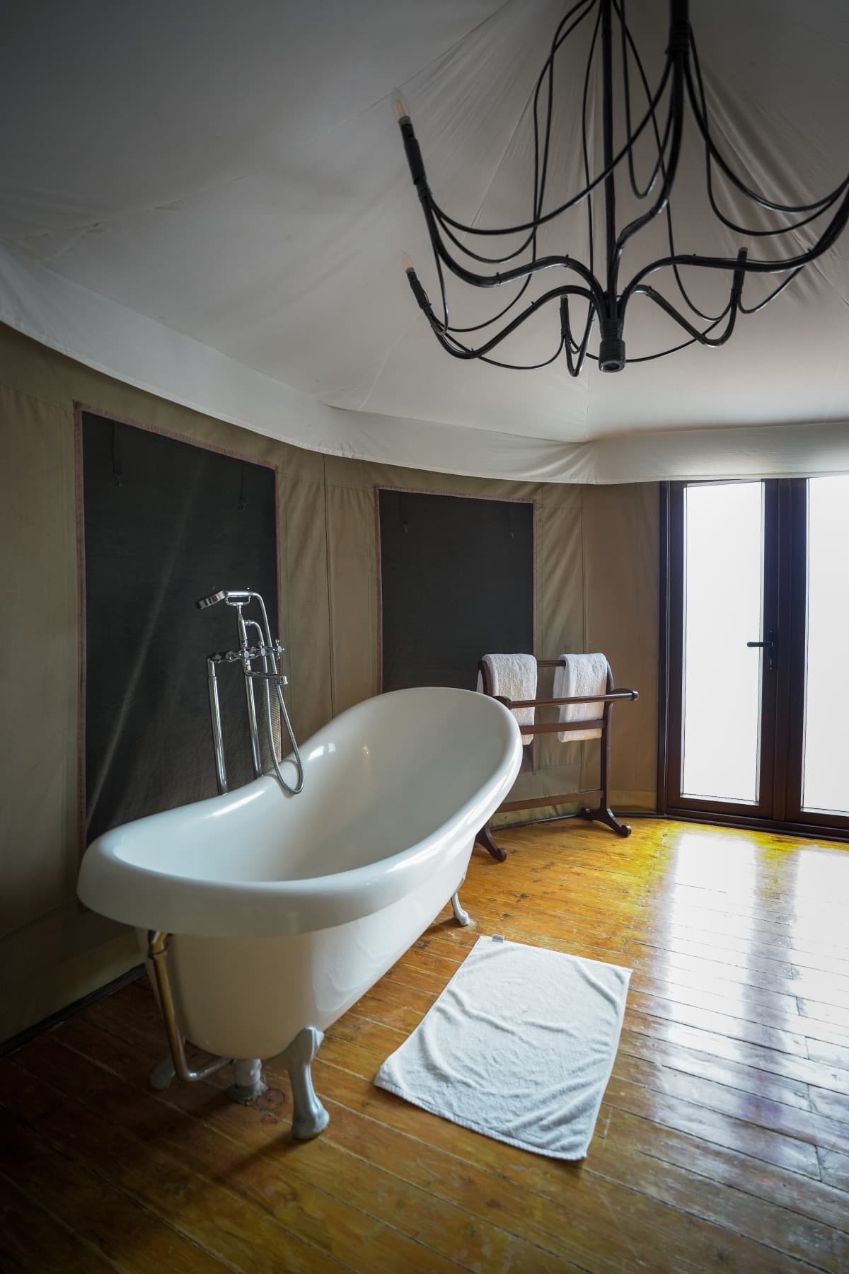 White clawfoot bathtub on a timber floor beside a bright glazed door