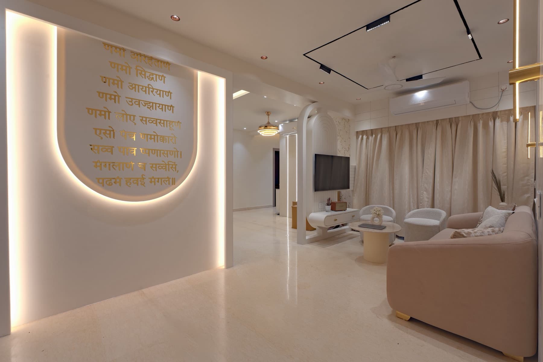 Backlit arched wall with gold Devanagari mantra lettering opening onto a living room