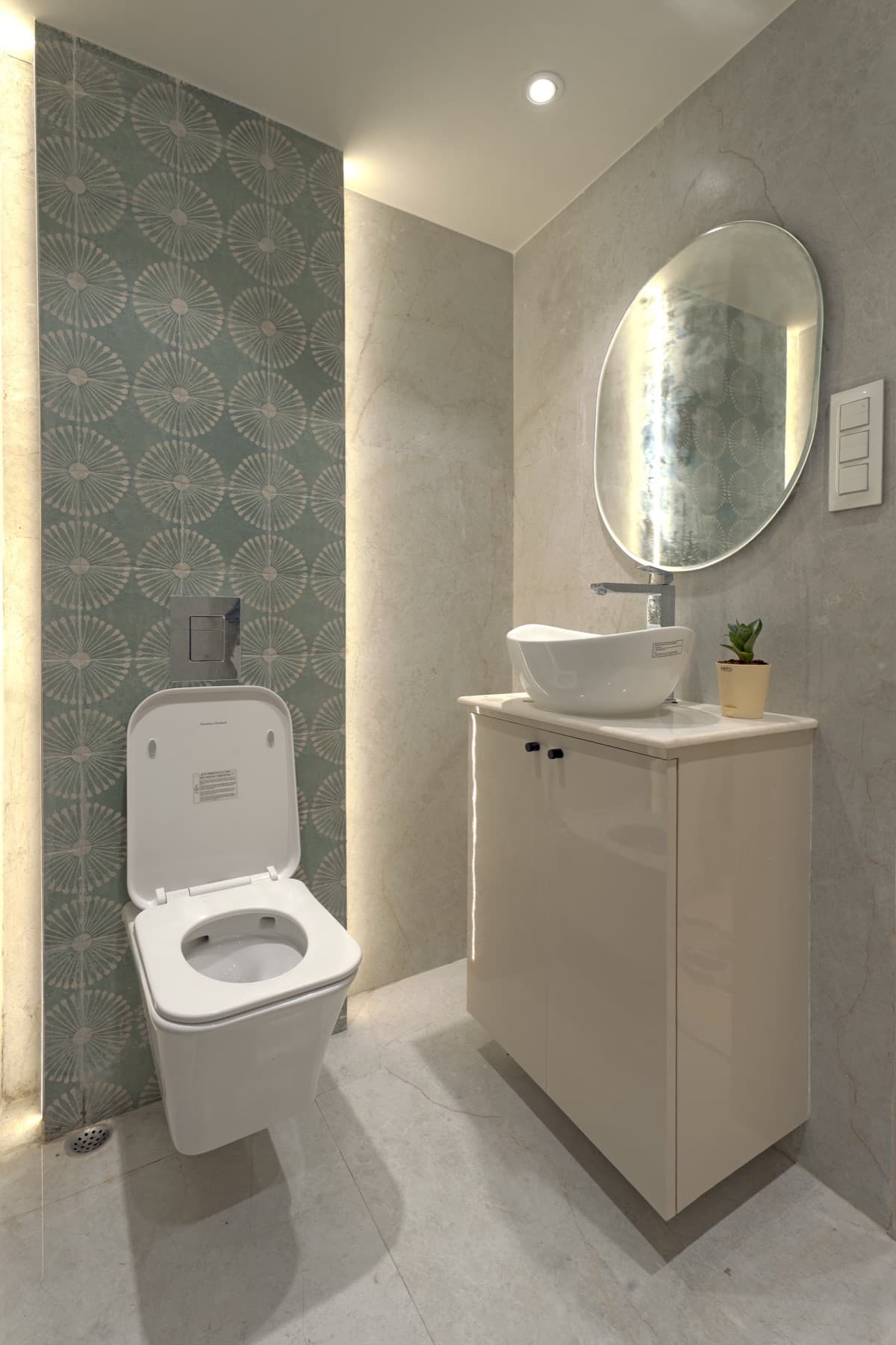 Compact powder room with wall-hung toilet, patterned green tile strip and oval lit mirror