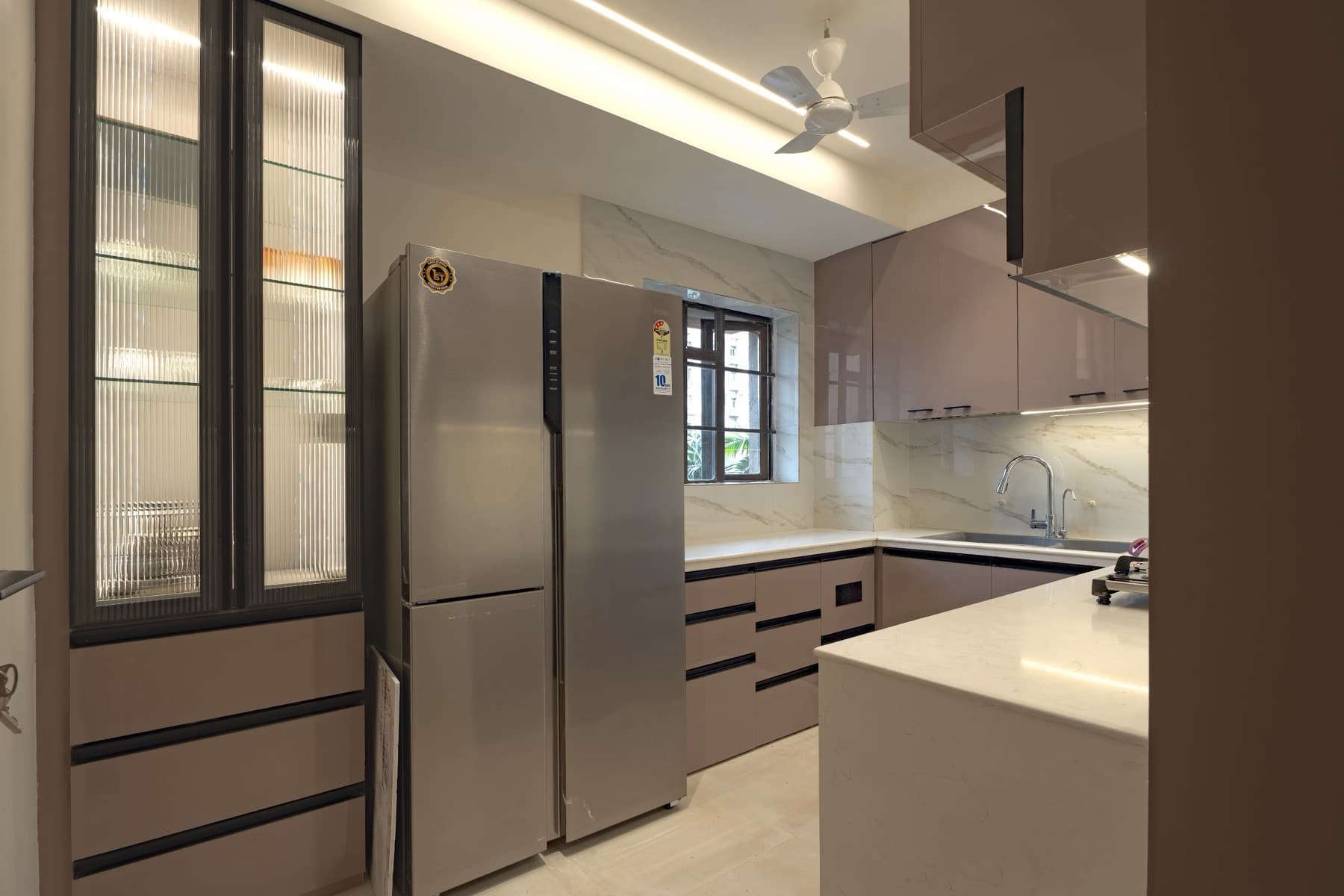 Modular kitchen with steel side-by-side fridge, glossy taupe cabinets and marble backsplash