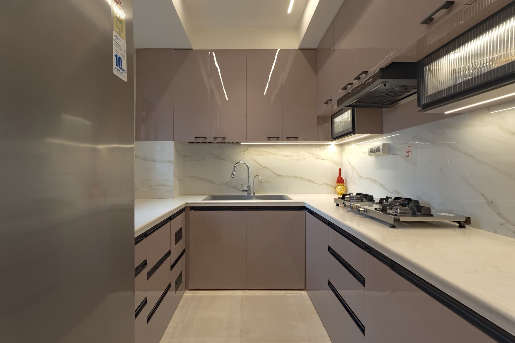 U-shaped kitchen with sink, gas hob, taupe gloss cabinets and fridge at the left