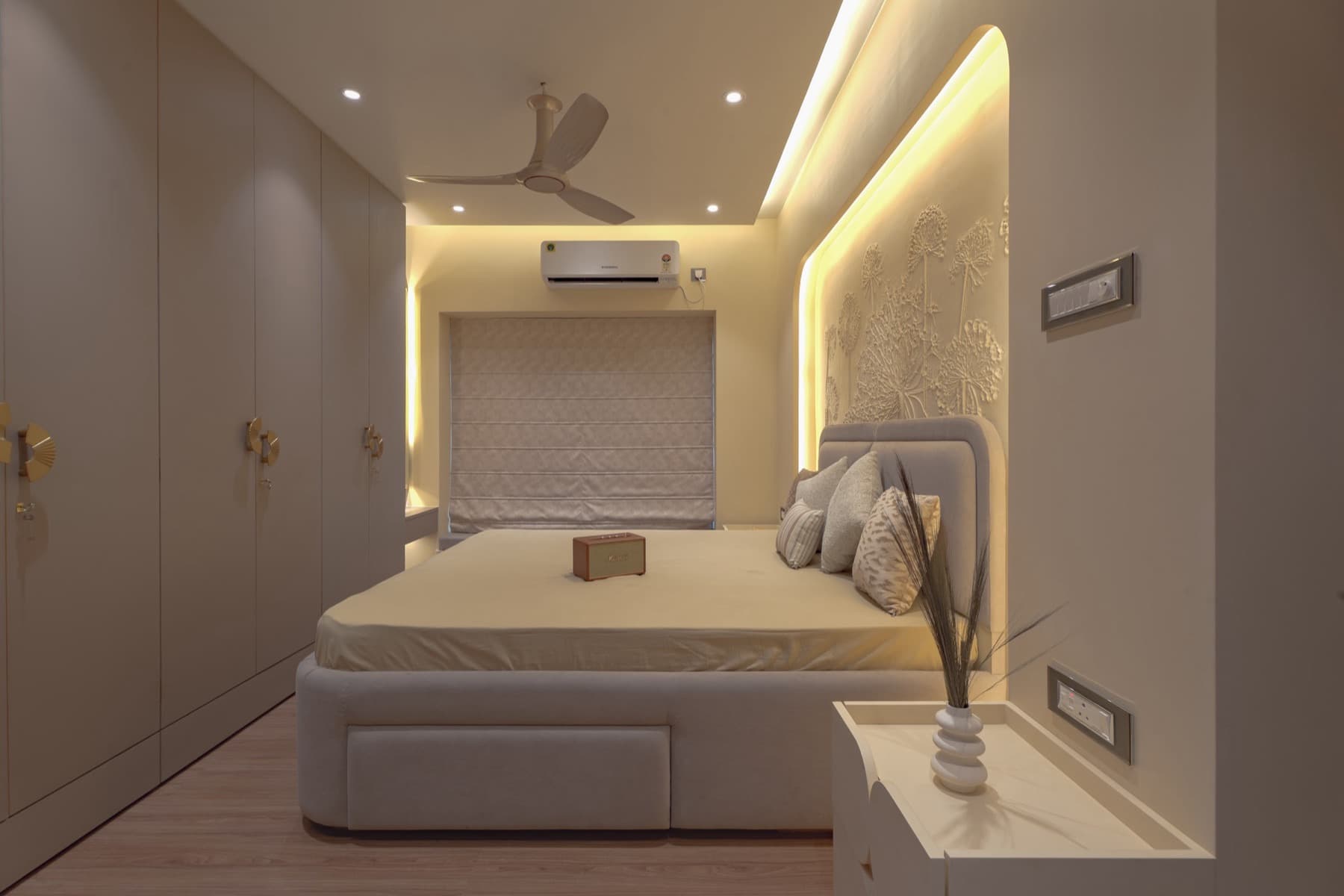 Bedroom down its length: wardrobe wall, upholstered bed and backlit relief headboard