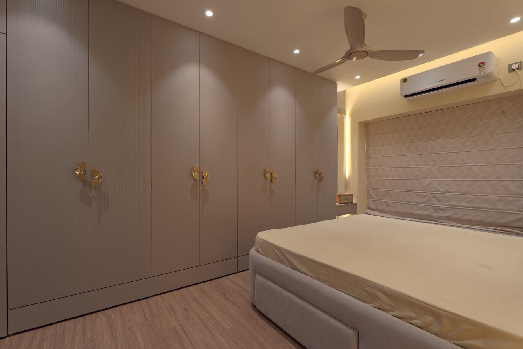 Floor-to-ceiling bedroom wardrobes with gold handles beside the corner of a bed