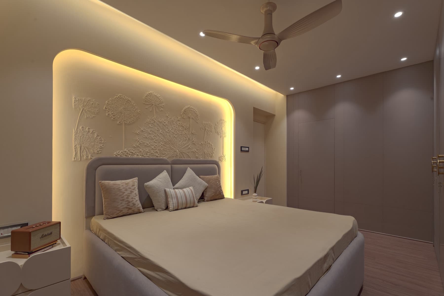 Bedroom with backlit dandelion plaster relief, grey headboard and cushioned bed