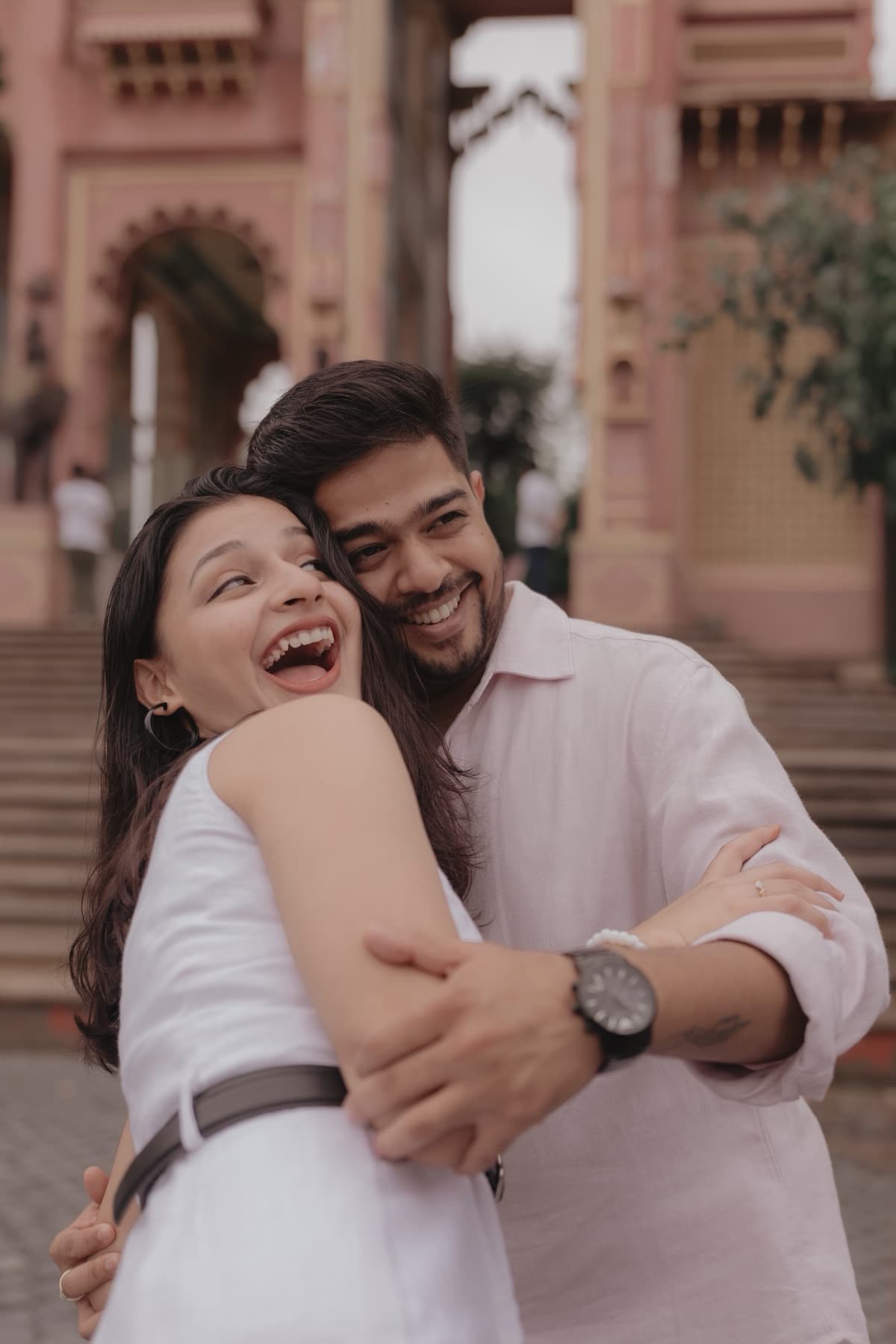 Laughing couple embracing in front of a pink heritage building