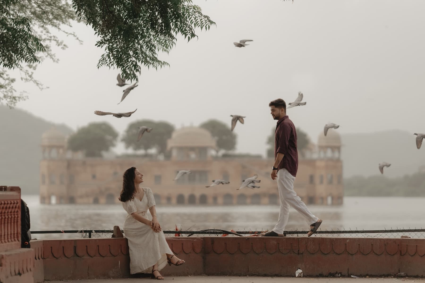 Couple on a lake parapet with pigeons in flight and a palace on the water behind