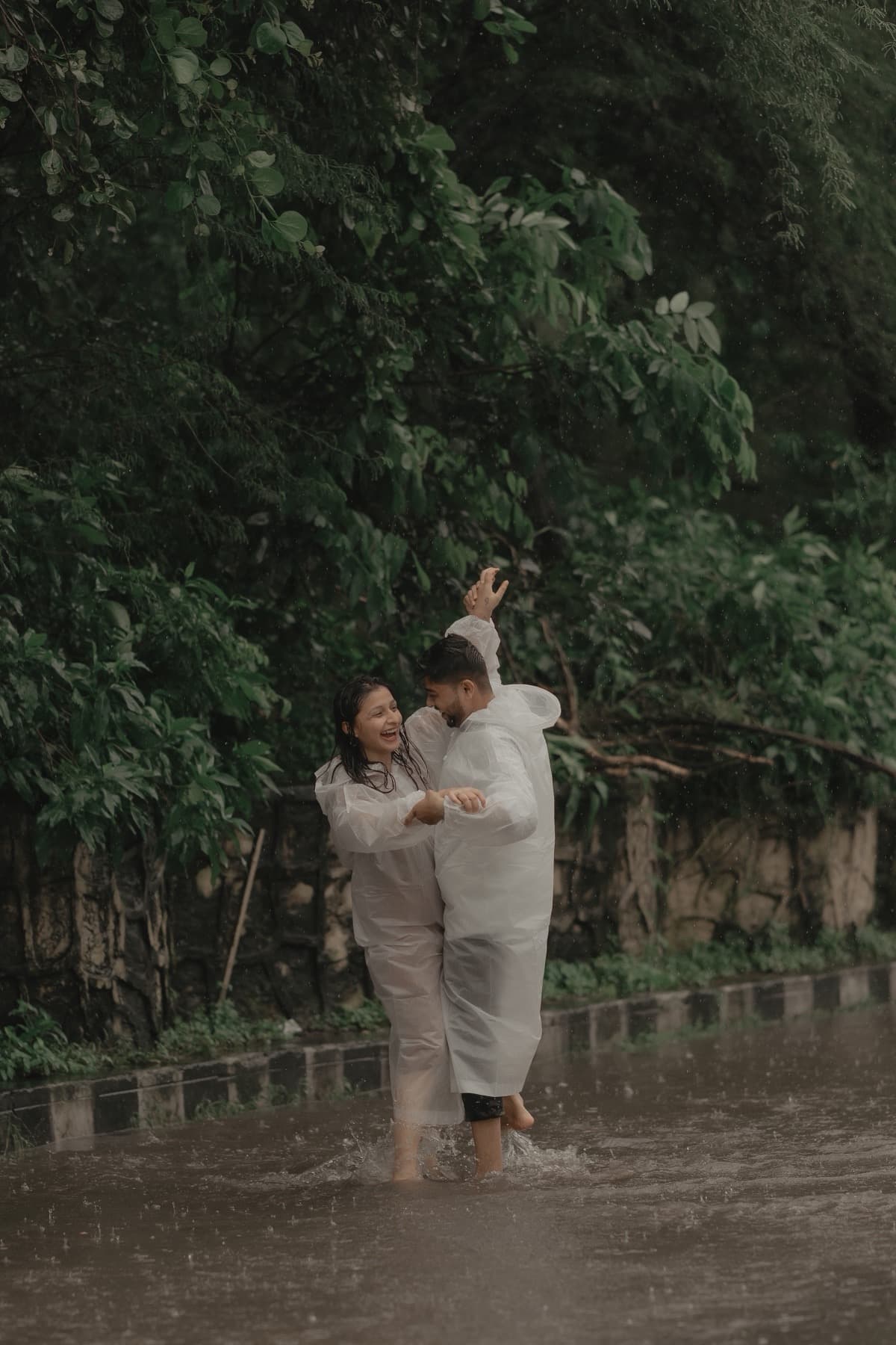 Couple dancing in the rain in clear ponchos against dense green foliage