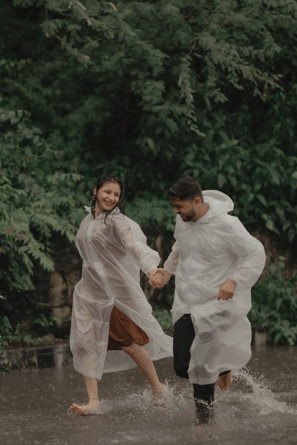 Couple running hand in hand through a puddle in the rain, water splashing