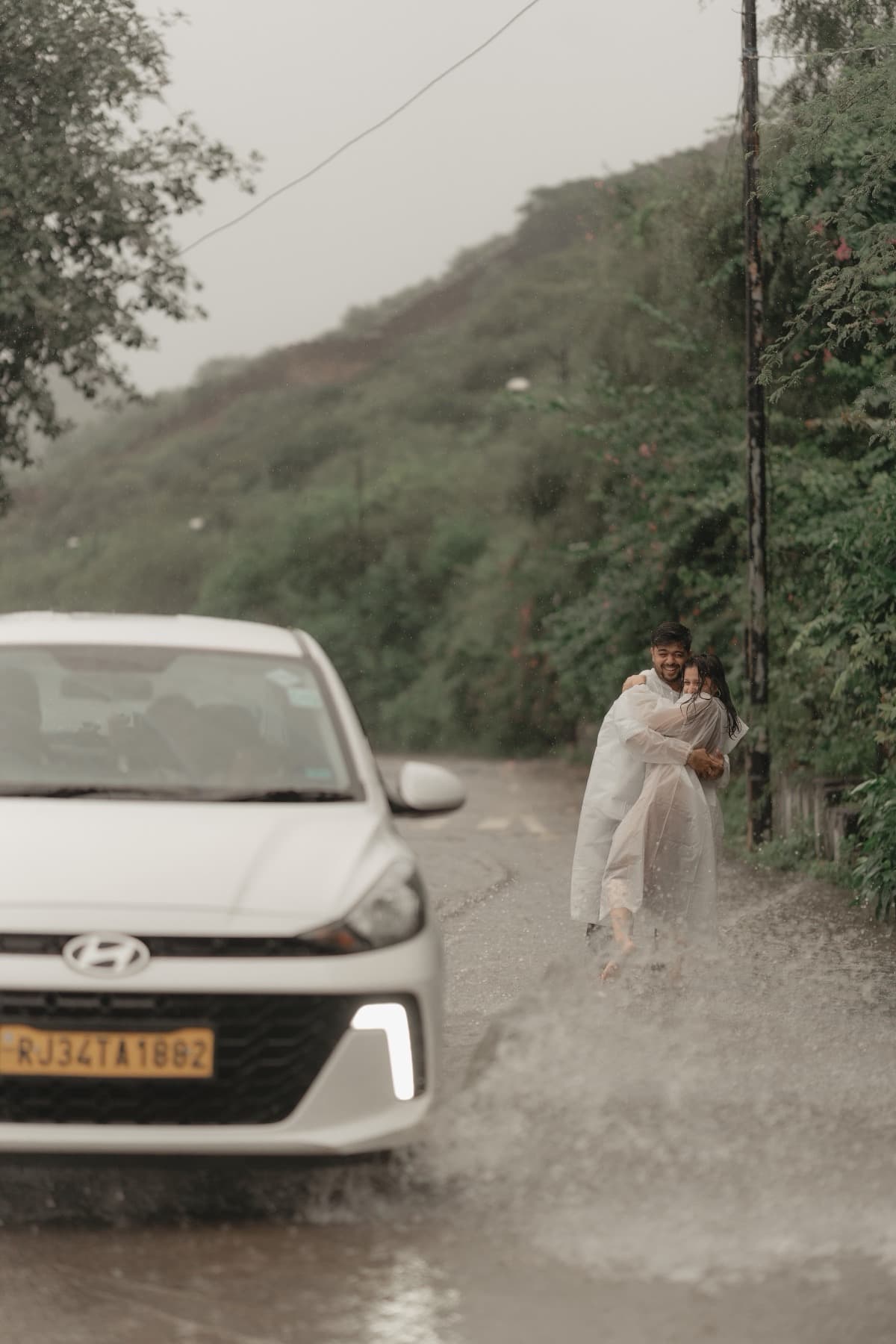 White car in the foreground of a flooded road with a couple embracing beyond it