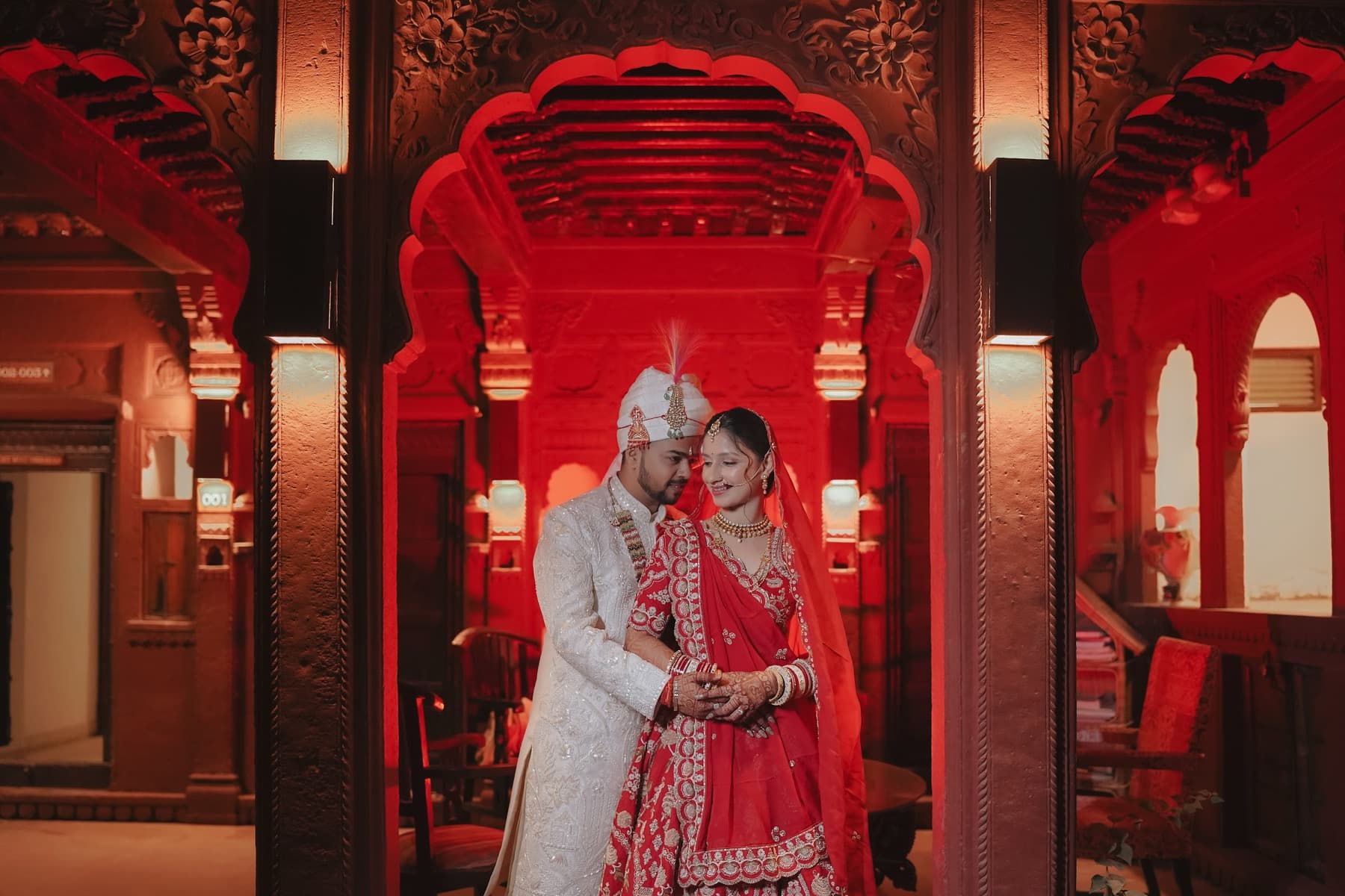 Couple forehead to forehead under an ornate carved arch washed in red light