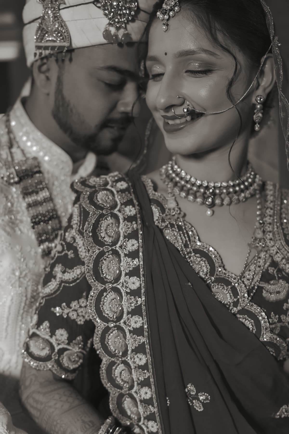Black-and-white close two-shot of a smiling bride in kundan jewellery resting against the groom