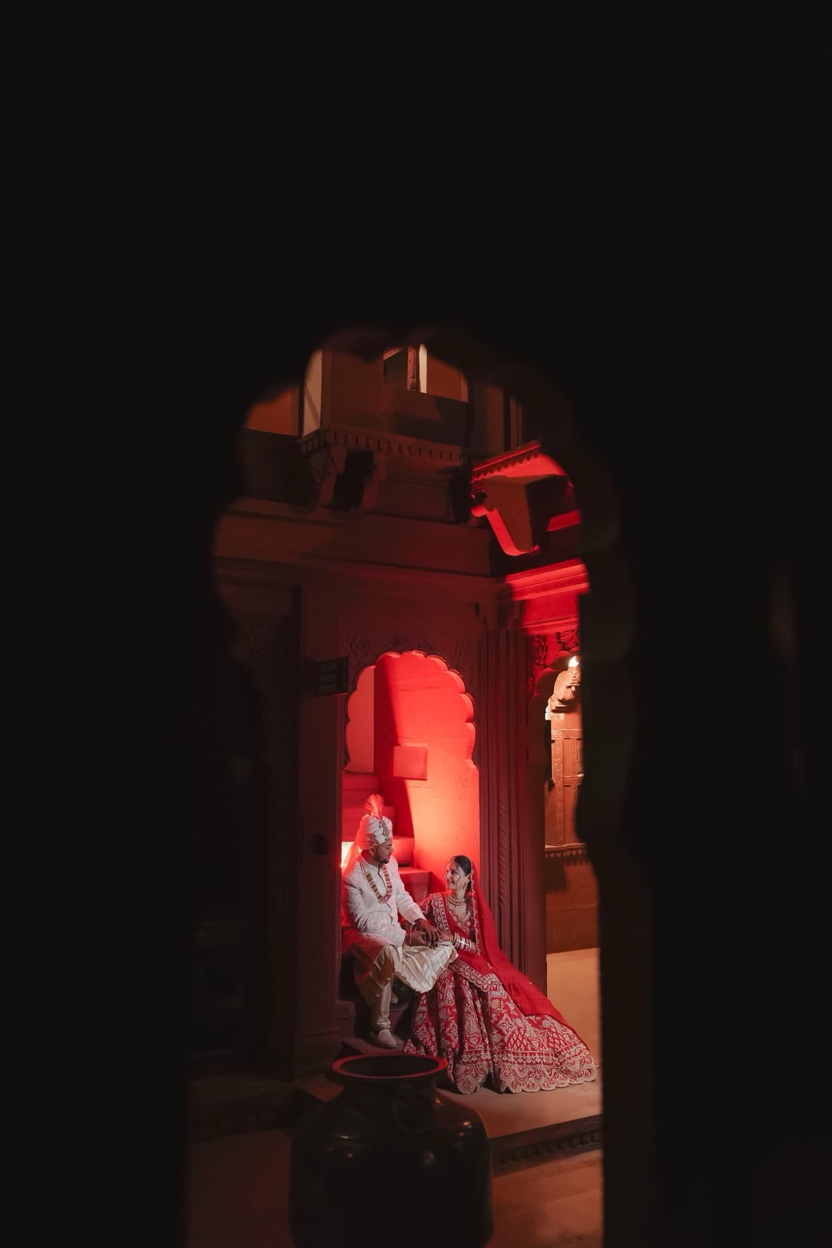 Distant couple glimpsed through a dark stone archway, lit red in a far alcove