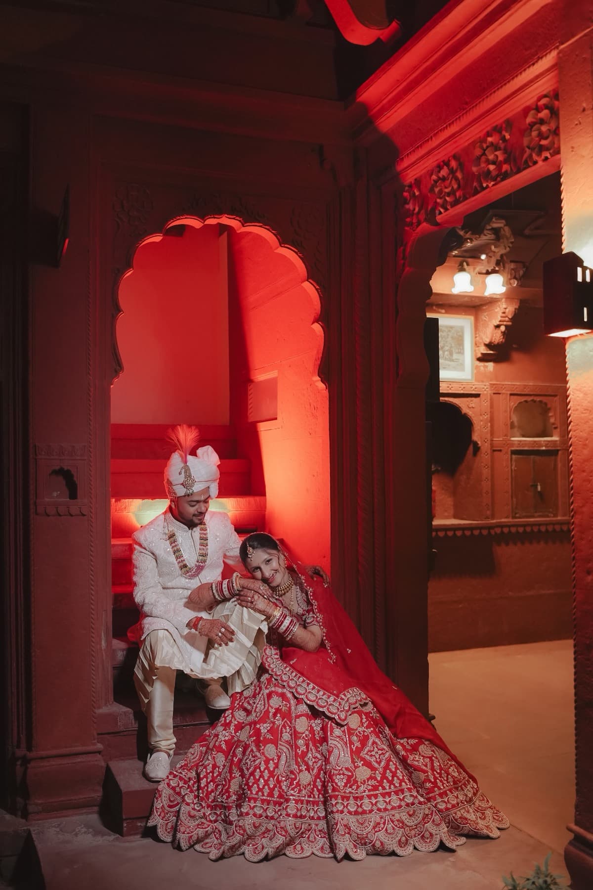 Couple seated in a red-lit alcove, bride leaning on the groom's shoulder