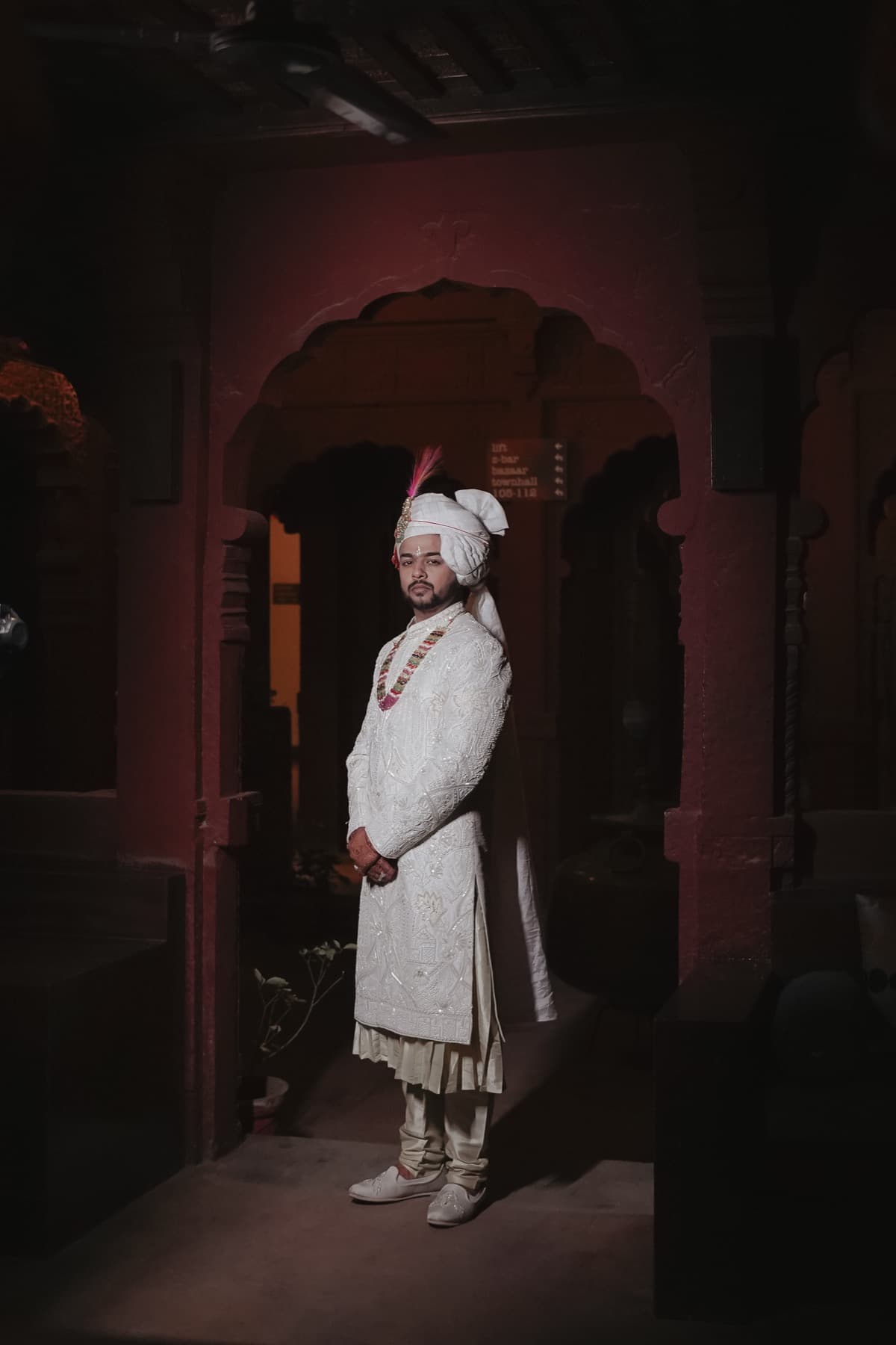 Groom in cream sherwani and turban standing full-length in a carved doorway