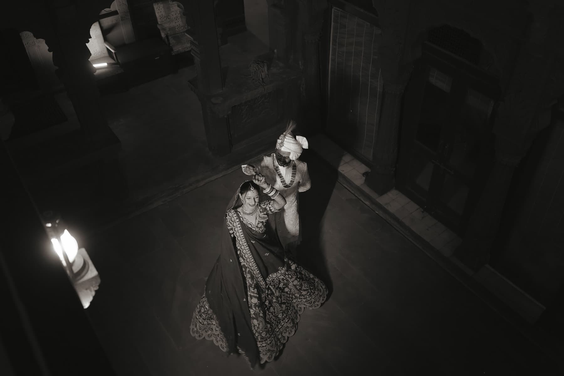 Overhead black-and-white view of a couple dancing alone in a dark stone courtyard