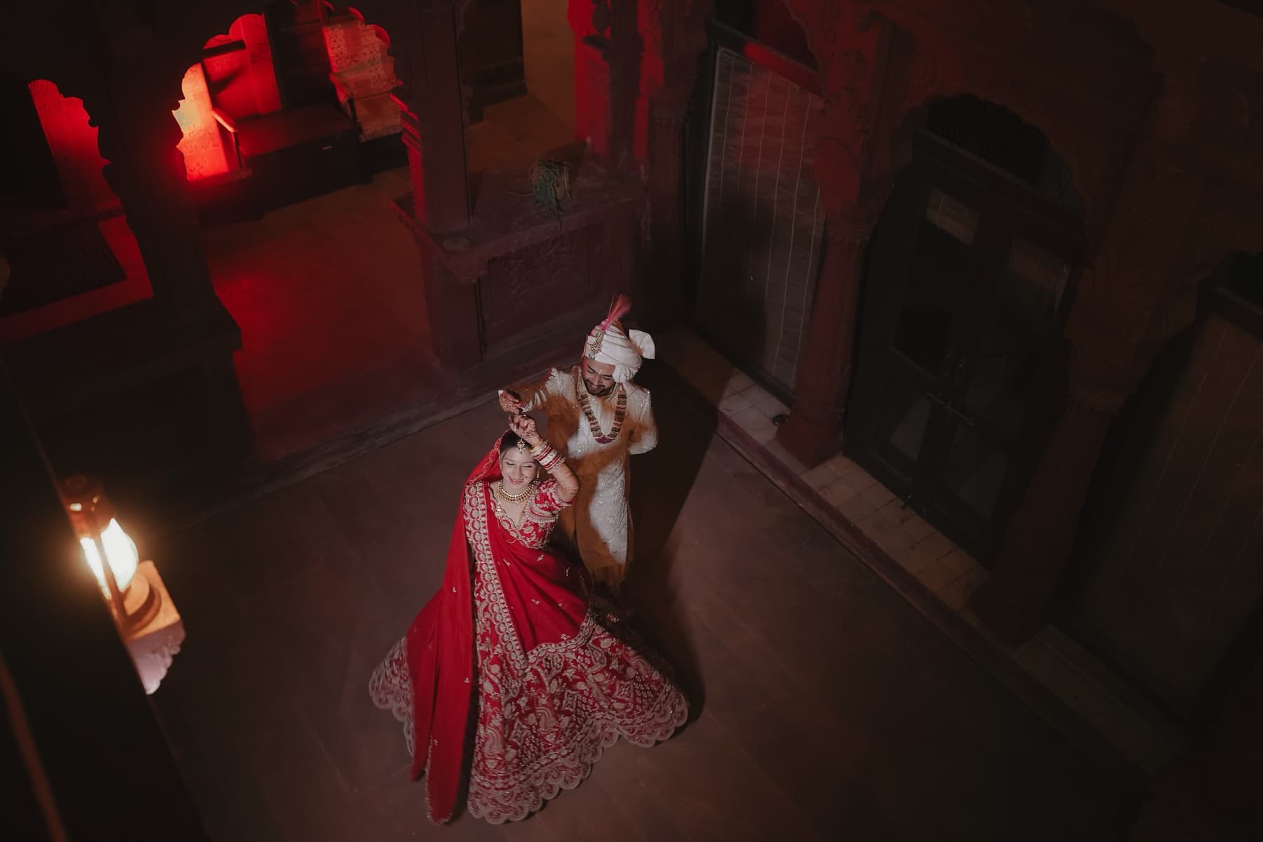 Overhead view of a couple dancing, the bride's red lehenga bright against dark stone