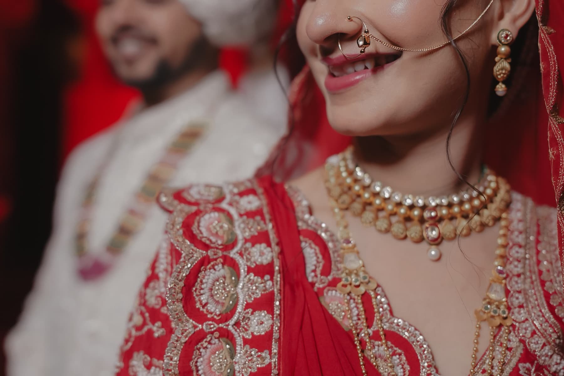 Tight crop on a laughing bride's nath, kundan necklaces and red embroidered blouse