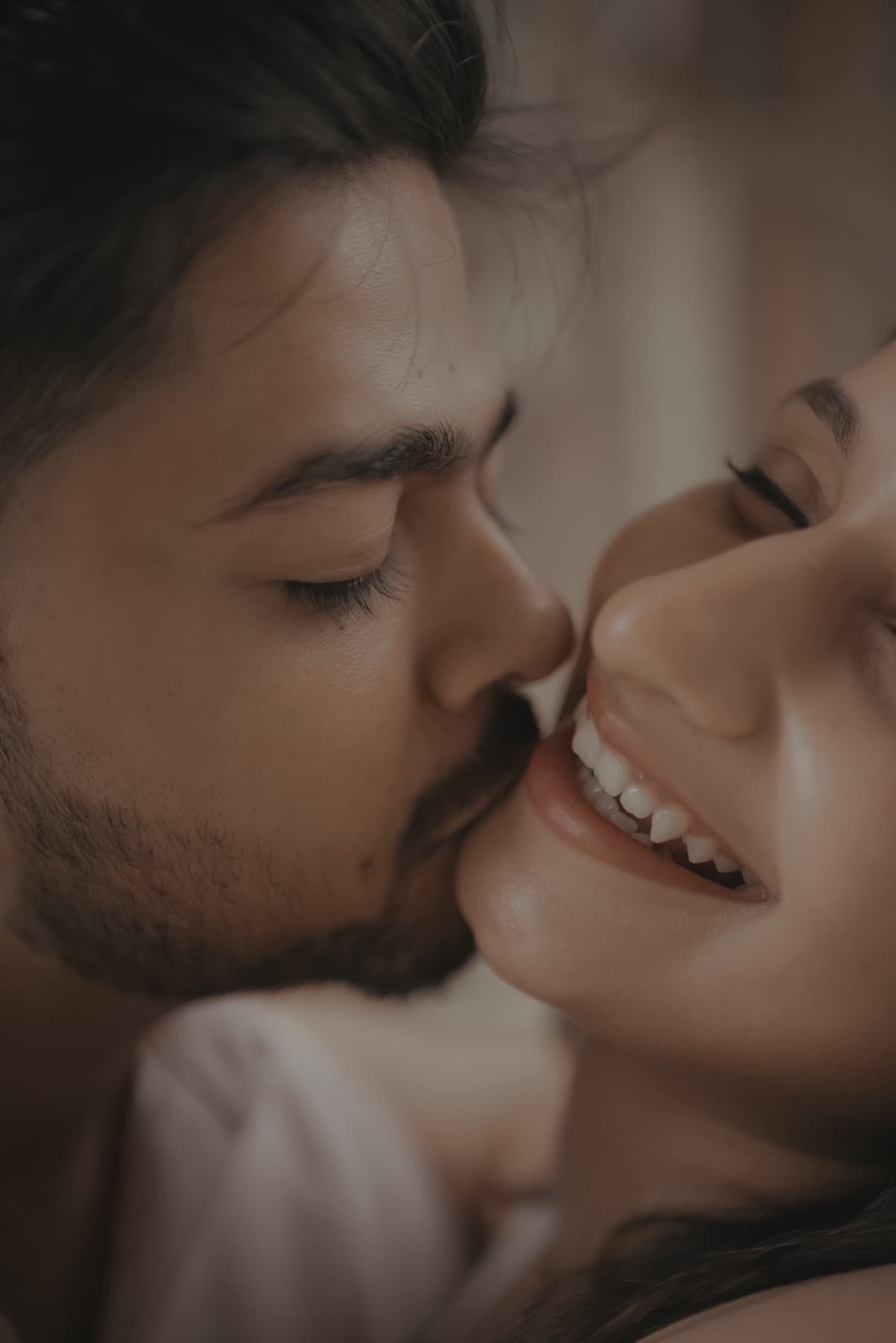 Extreme close-up of a man kissing a laughing woman on the cheek in soft warm light