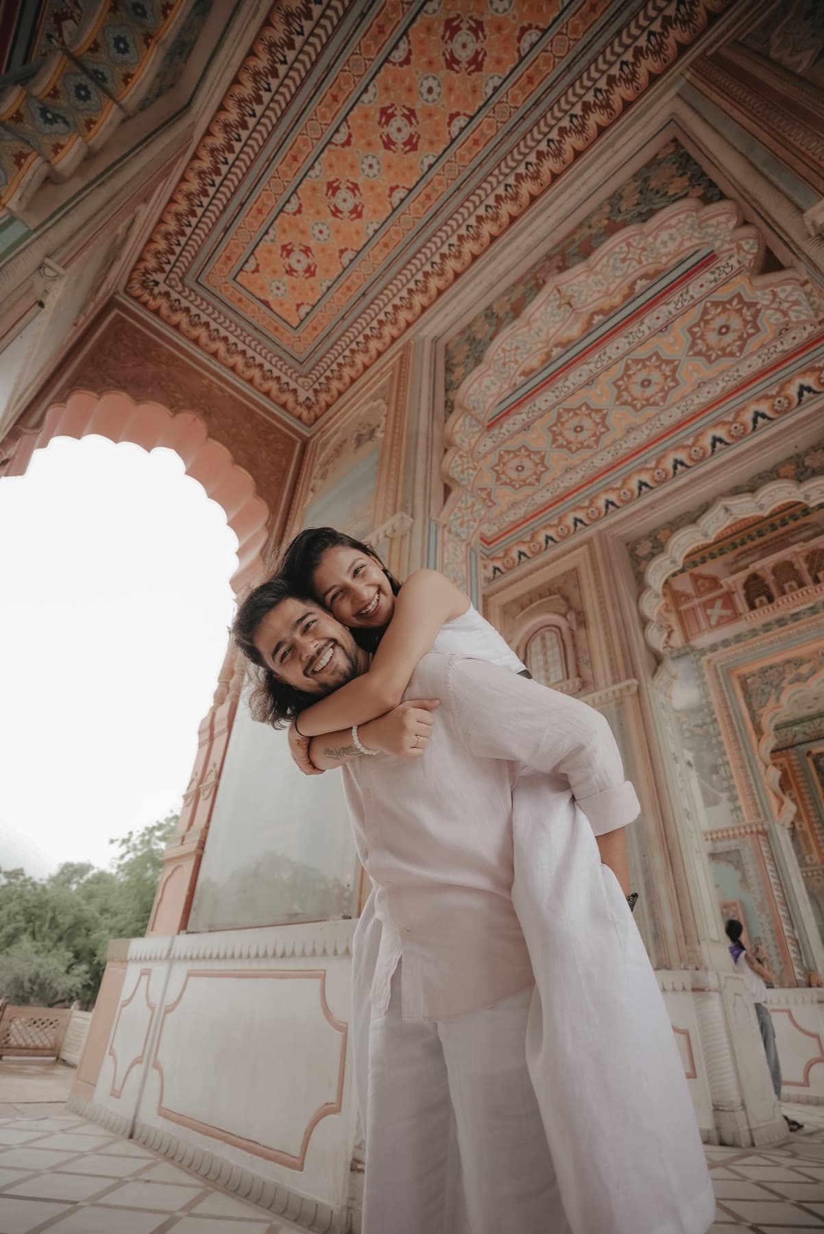 Man piggybacks a smiling woman beneath a painted scalloped archway