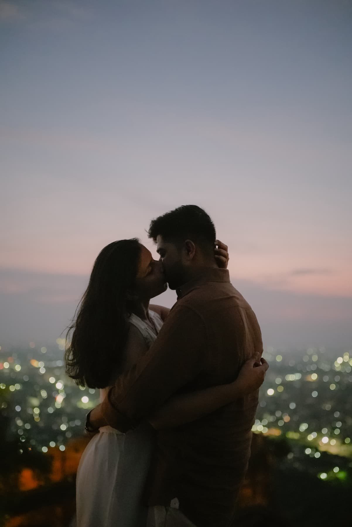 Silhouetted couple kissing at dusk above a bokeh city skyline