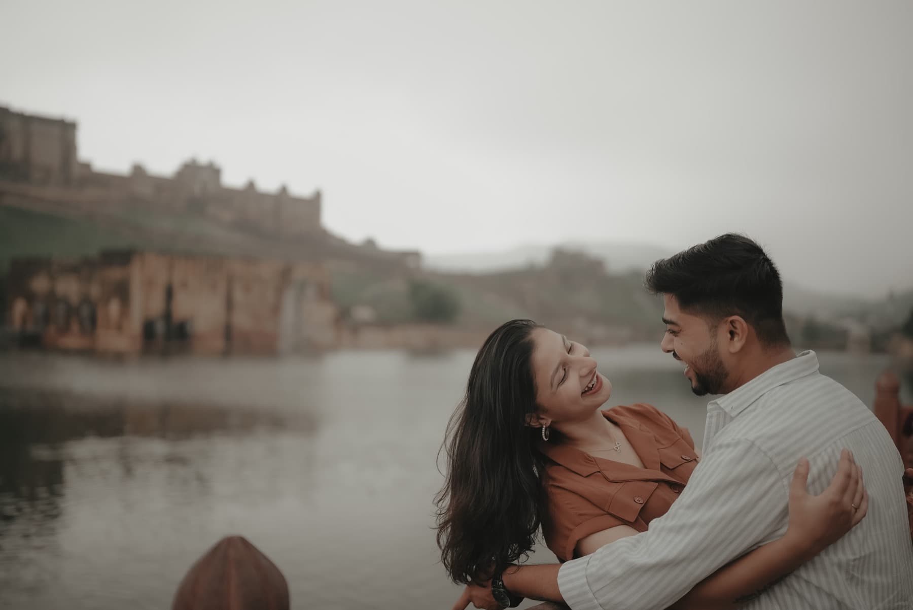 Couple laughing face to face beside a misty lake below hilltop fort ramparts