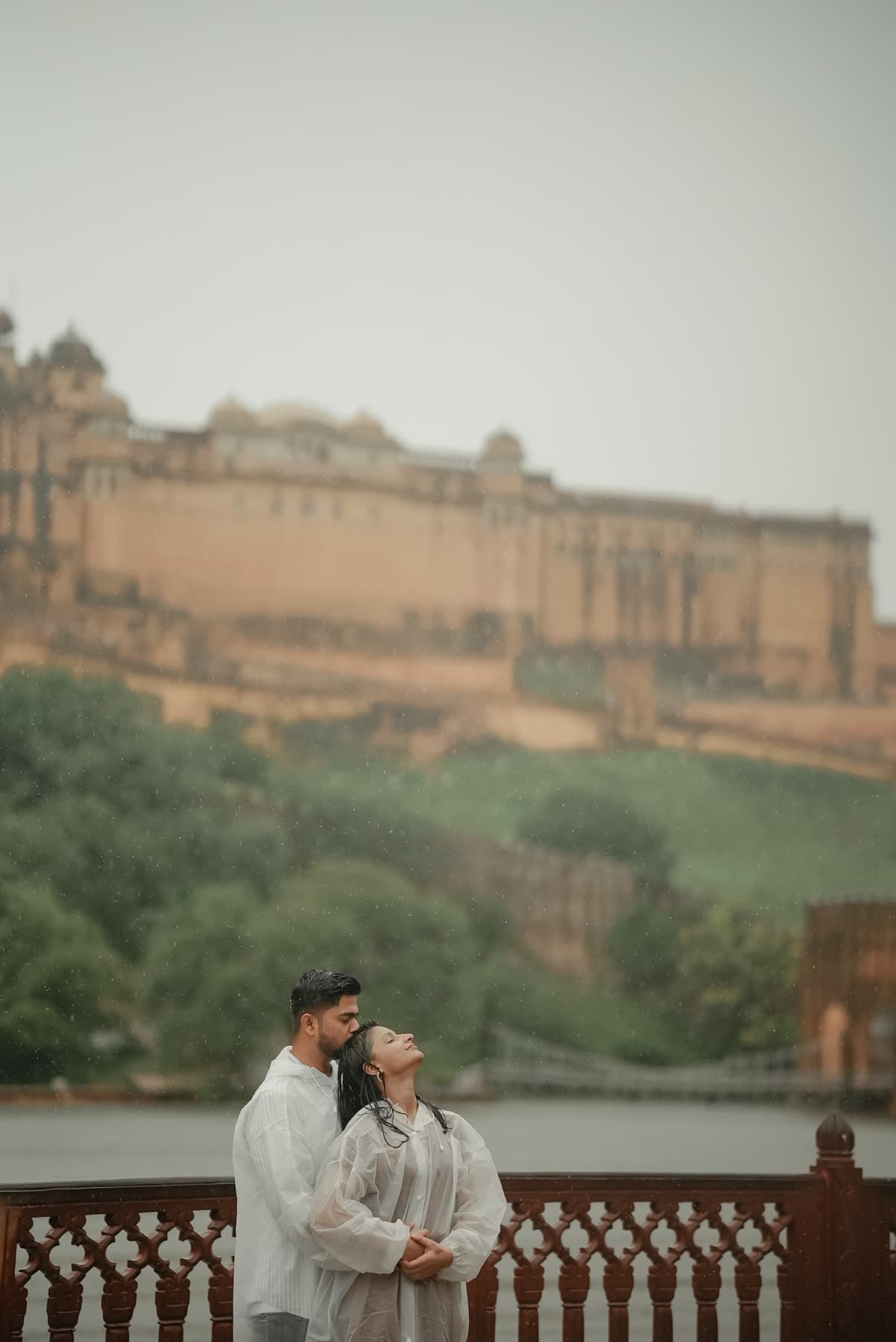 Small figures of a couple in rain on a terrace beneath a vast hilltop fort