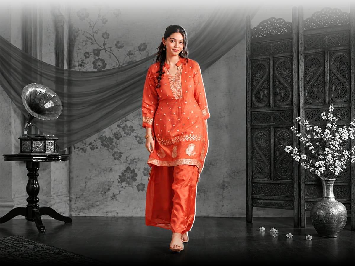 Woman in an orange embroidered kurta set beside a gramophone and a carved screen