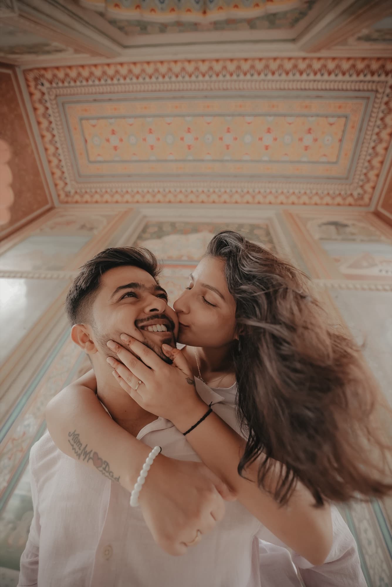 Woman kisses a laughing man on the cheek as he carries her under a frescoed ceiling