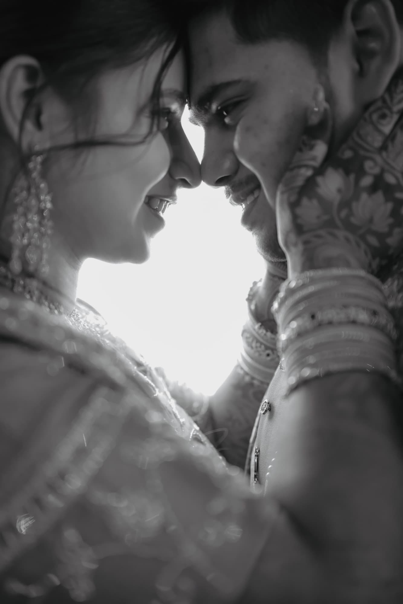 Black and white close-up of a bride and groom touching foreheads, her mehendi hand on his face