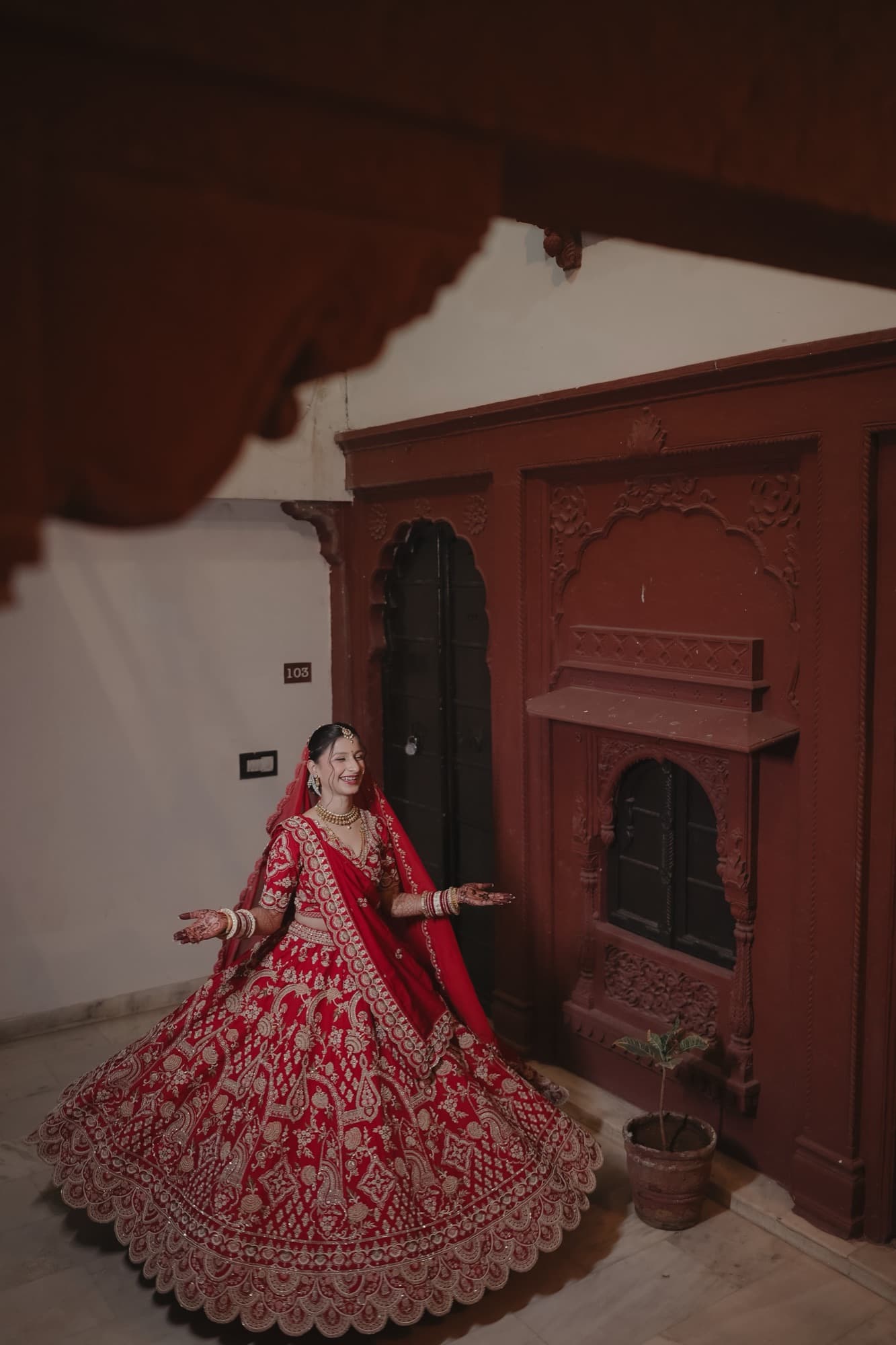 Bride twirling in a flared red and gold lehenga in a carved haveli room
