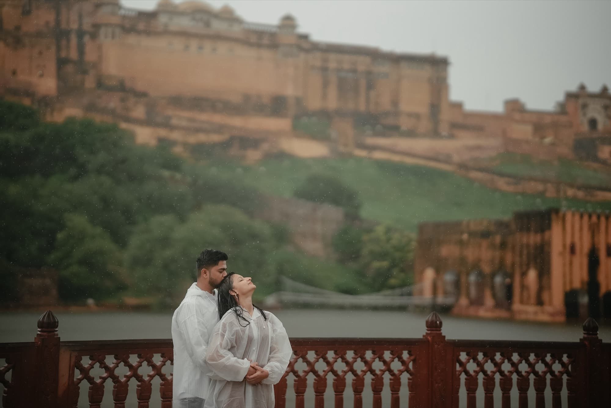 Couple in white embracing in the rain on a carved terrace below a hilltop fort