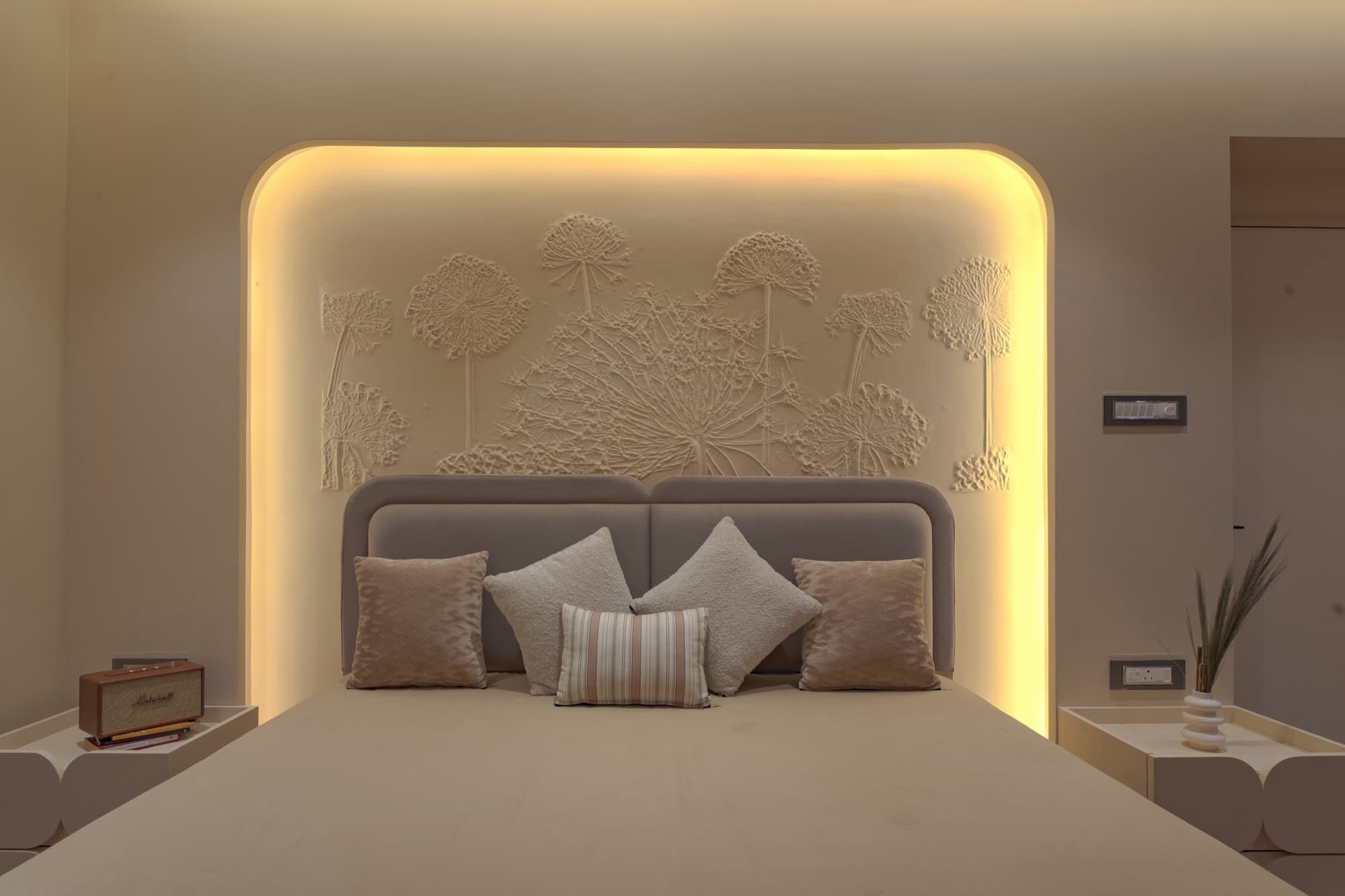 Symmetrical bed head-on beneath a backlit plaster relief panel
